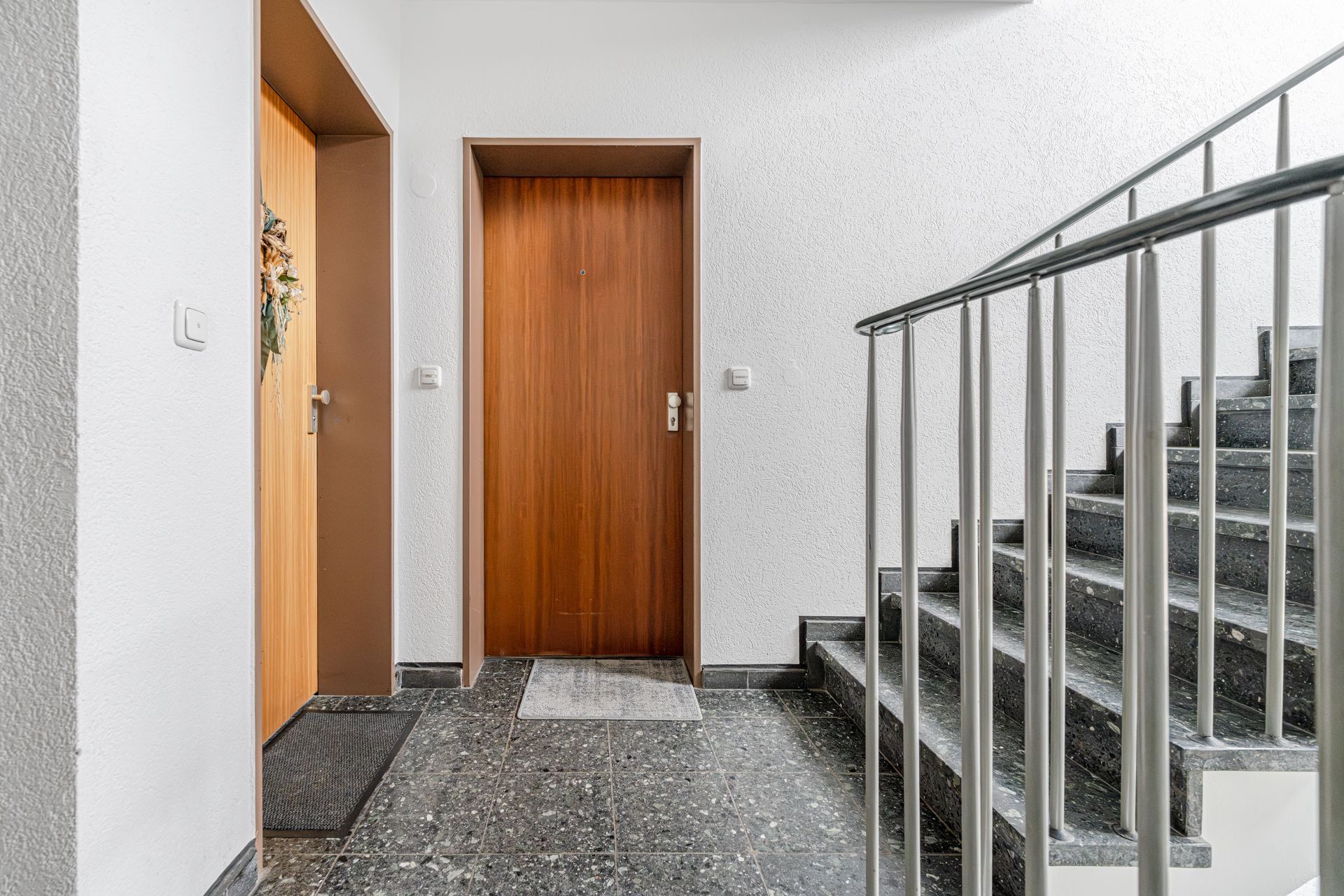 Flur mit zwei Wohnungstüren und einer Treppe mit Metallgeländer.