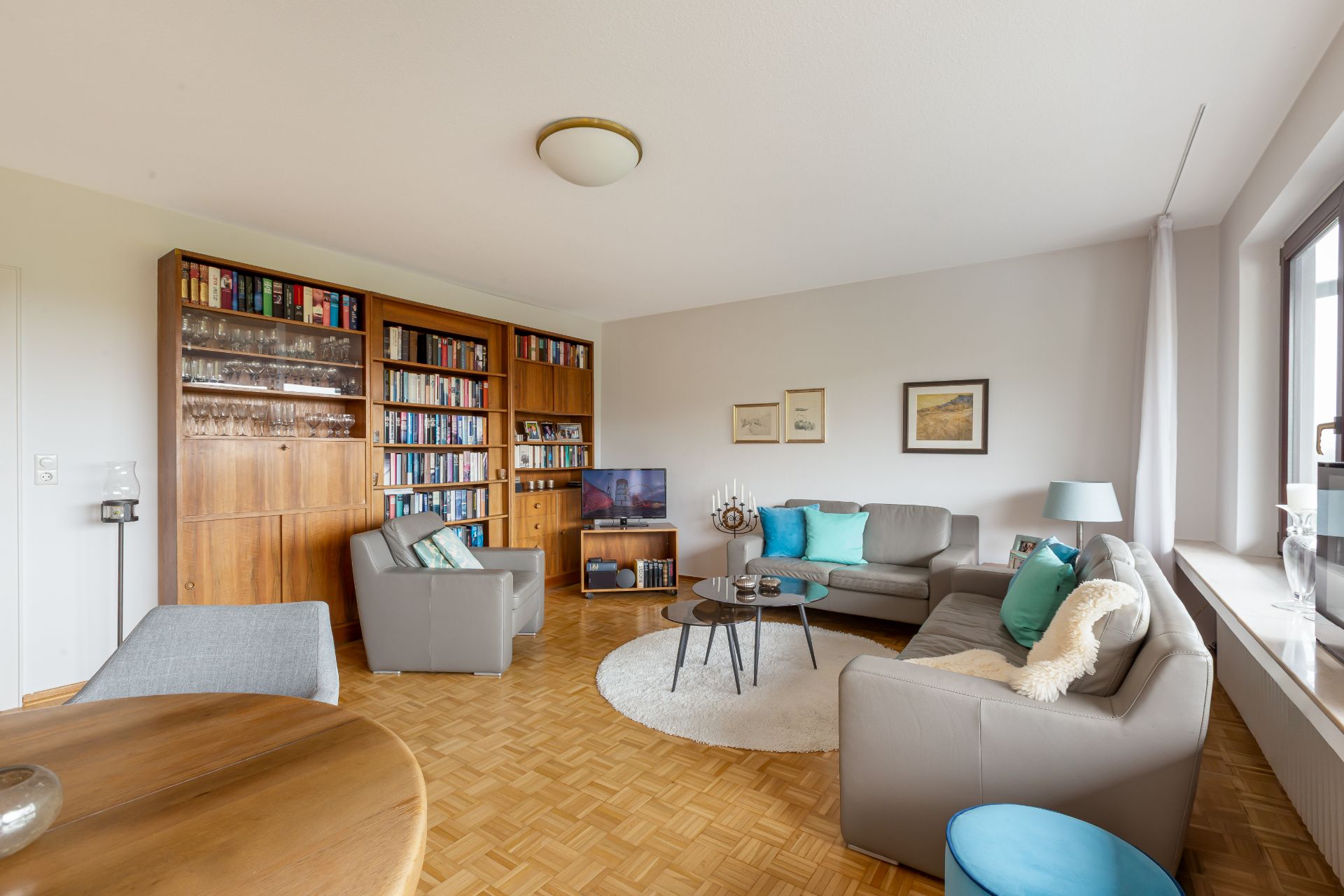 Helles Wohnzimmer mit grauen Sofas, Bücherregal, Couchtisch und großem Fenster.