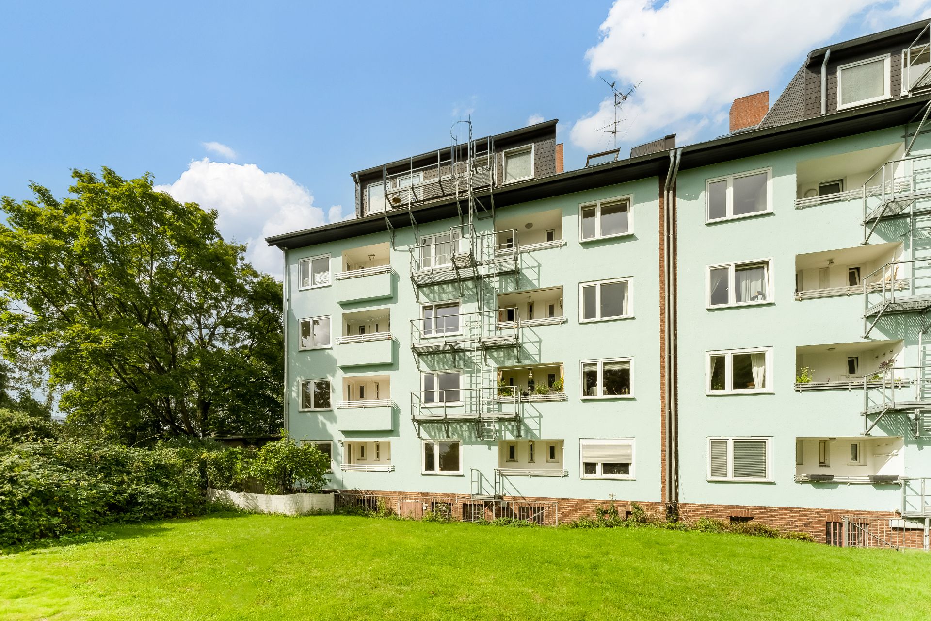 Mehrfamilienhaus mit Balkonen und grünem Rasen vor dem Gebäude bei sonnigem Wetter.
