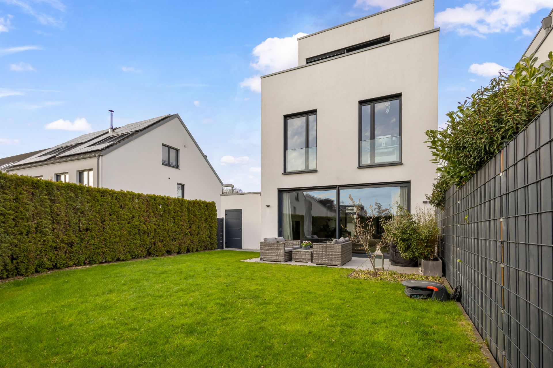 Modernes weißes Wohnhaus mit Garten, Hecke und Terrasse mit Sitzgruppe.