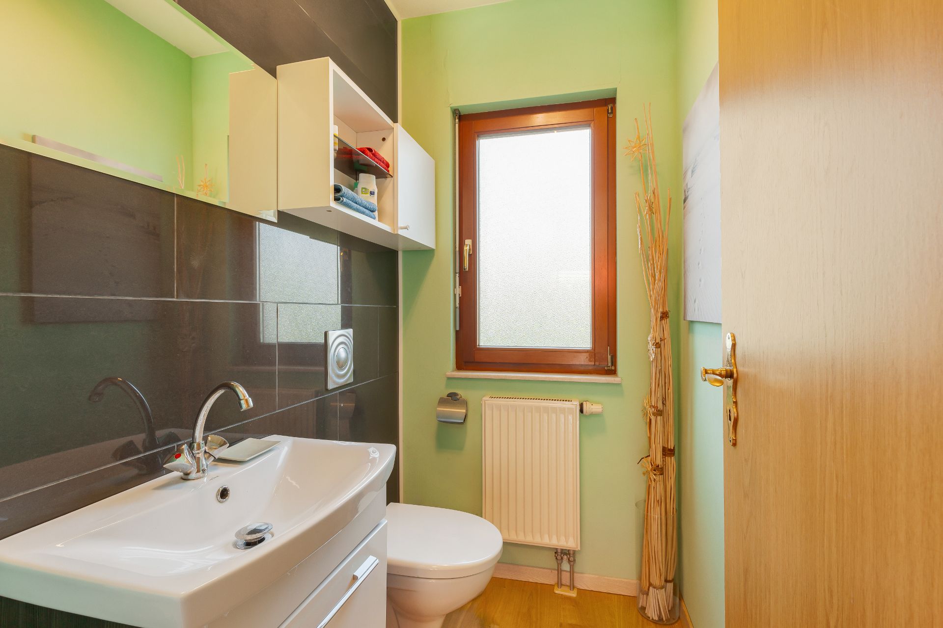 Kleines Badezimmer mit Waschbecken, Toilette, Fenster und grün gestrichenen Wänden.