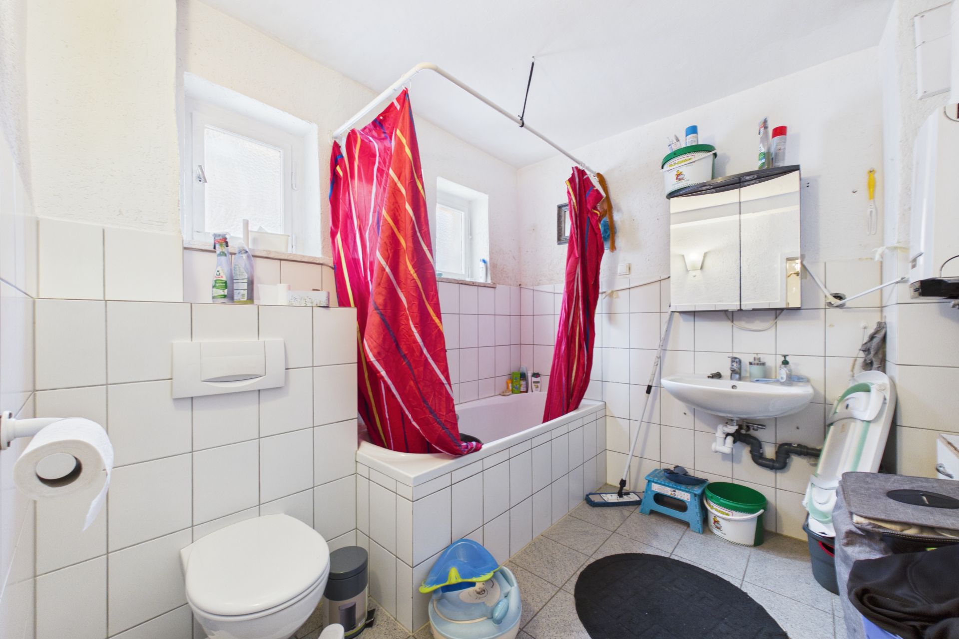 Badezimmer mit Badewanne, rotem Duschvorhang, WC, Waschbecken und Spiegelschrank.