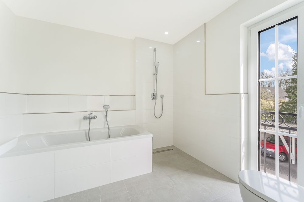 Helles Badezimmer mit Badewanne, Dusche und Fenster mit Blick nach draußen.