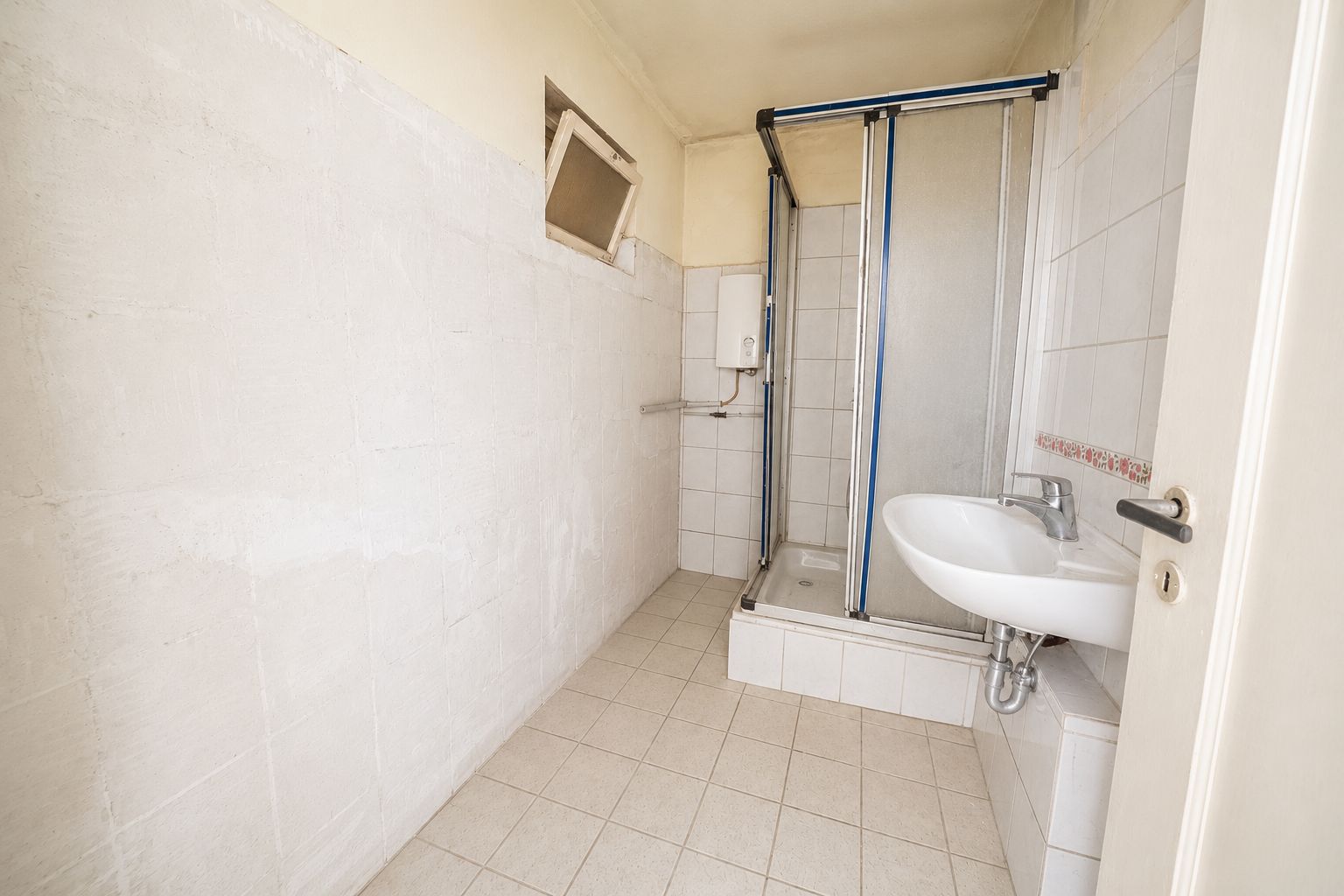 Ein einfaches Badezimmer mit Dusche, Waschbecken und kleinem Fenster.