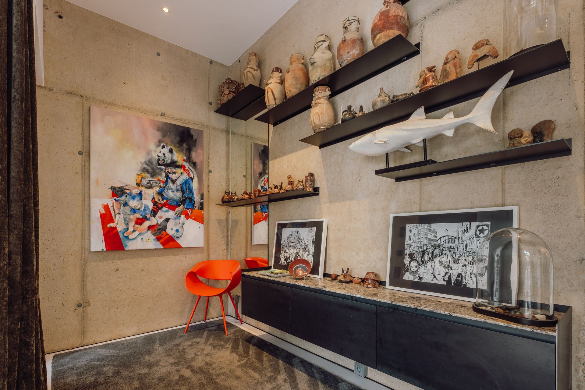 Wohnzimmer mit Kunstwerken, Regalen mit Keramik, einem roten Stuhl und Dekorationsobjekten.
