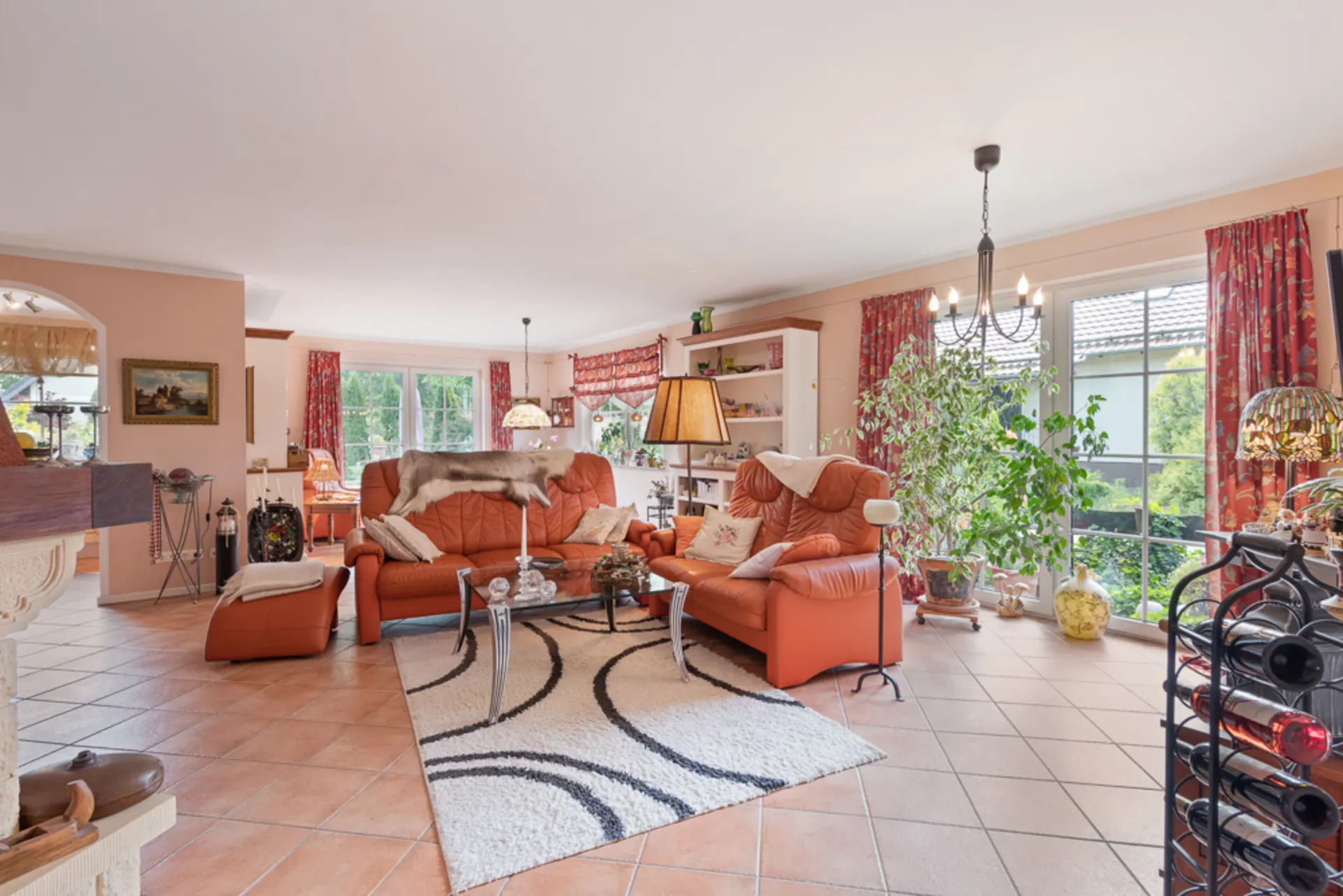 Wohnzimmer mit orangefarbenen Sofas, großem Fenster, Pflanzen und Teppich auf Fliesenboden.