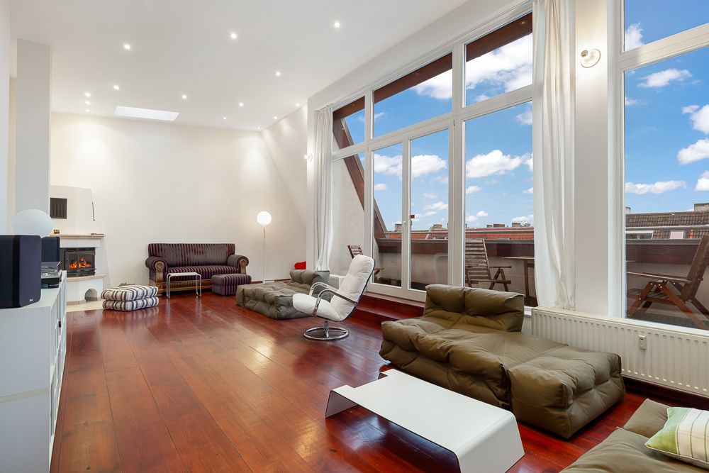 Helles Wohnzimmer mit großen Fenstern, Holzboden und modernen Sitzmöbeln.
