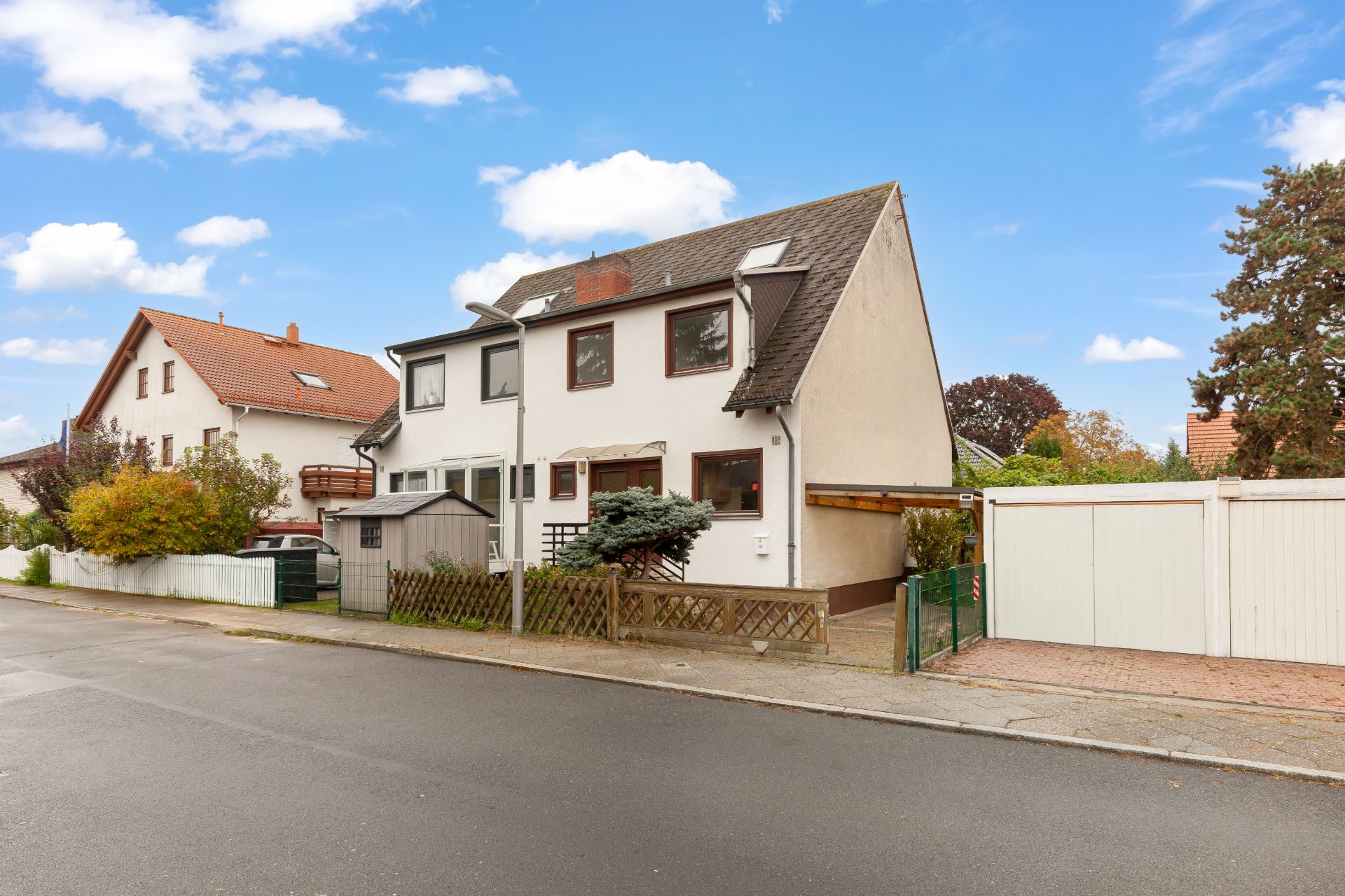 Doppelhaushälfte mit Vorgarten, Holzzaun und Carport an einer ruhigen Wohnstraße.