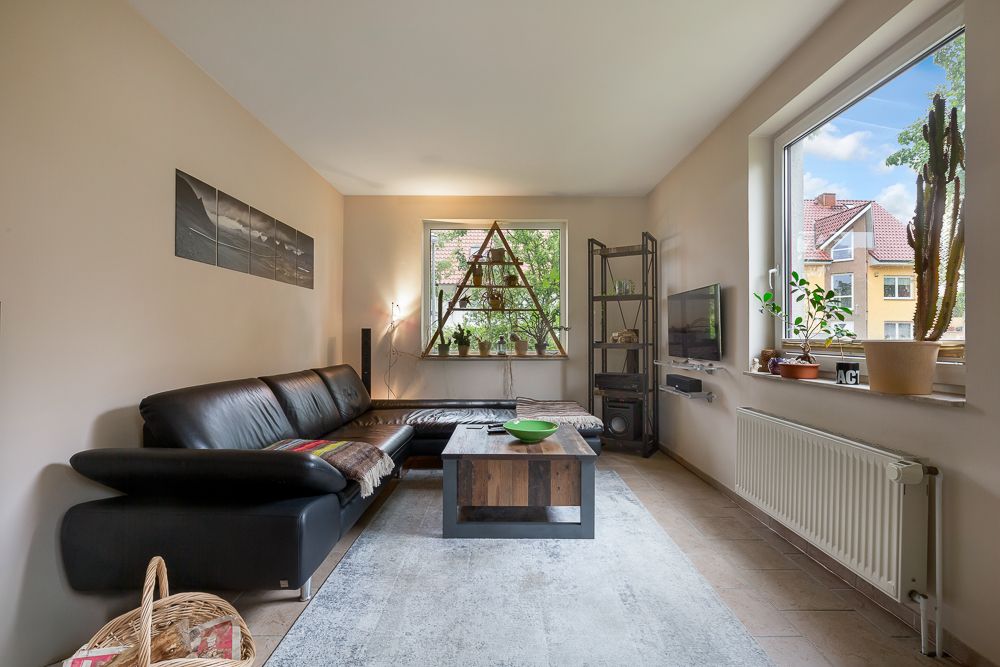 Helles Wohnzimmer mit schwarzem Sofa, Couchtisch, Pflanzen und großem Fenster.