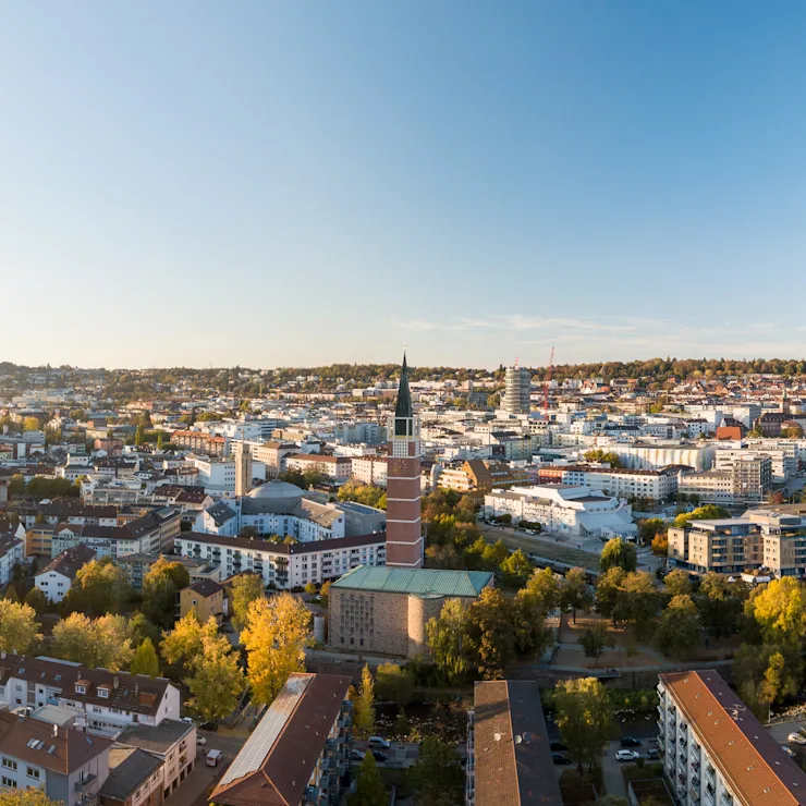 Luftaufnahme einer Stadt mit vielen Wohnhäusern, Bäumen und einer großen Kirche in der Mitte.