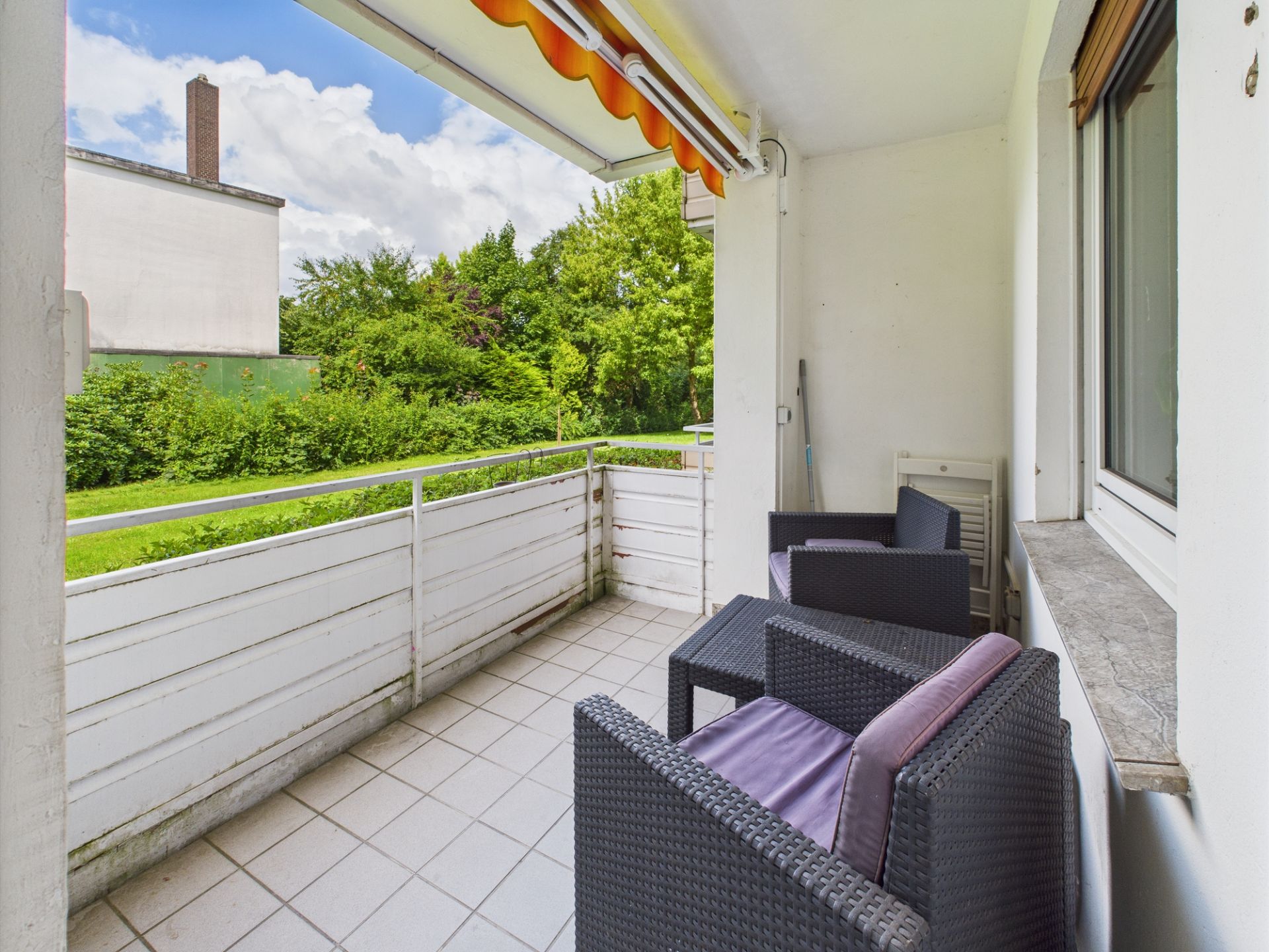 Überdachter Balkon mit zwei schwarzen Stühlen und Blick ins Grüne.