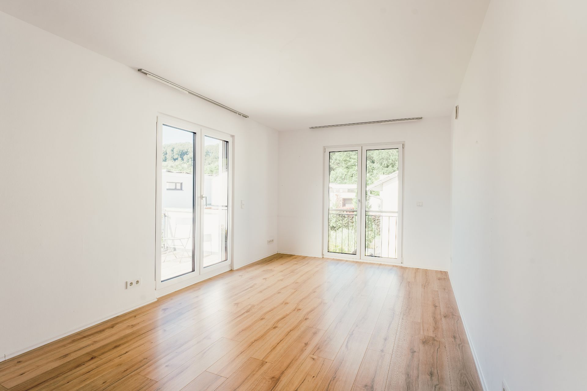 Heller, leerer Raum mit Holzboden und zwei großen Fenstertüren.