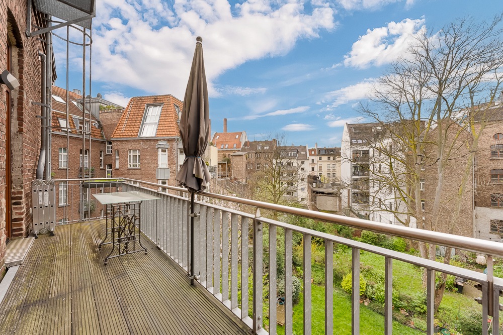 Balkon mit Tisch und Sonnenschirm, Blick auf Garten und benachbarte Wohnhäuser.