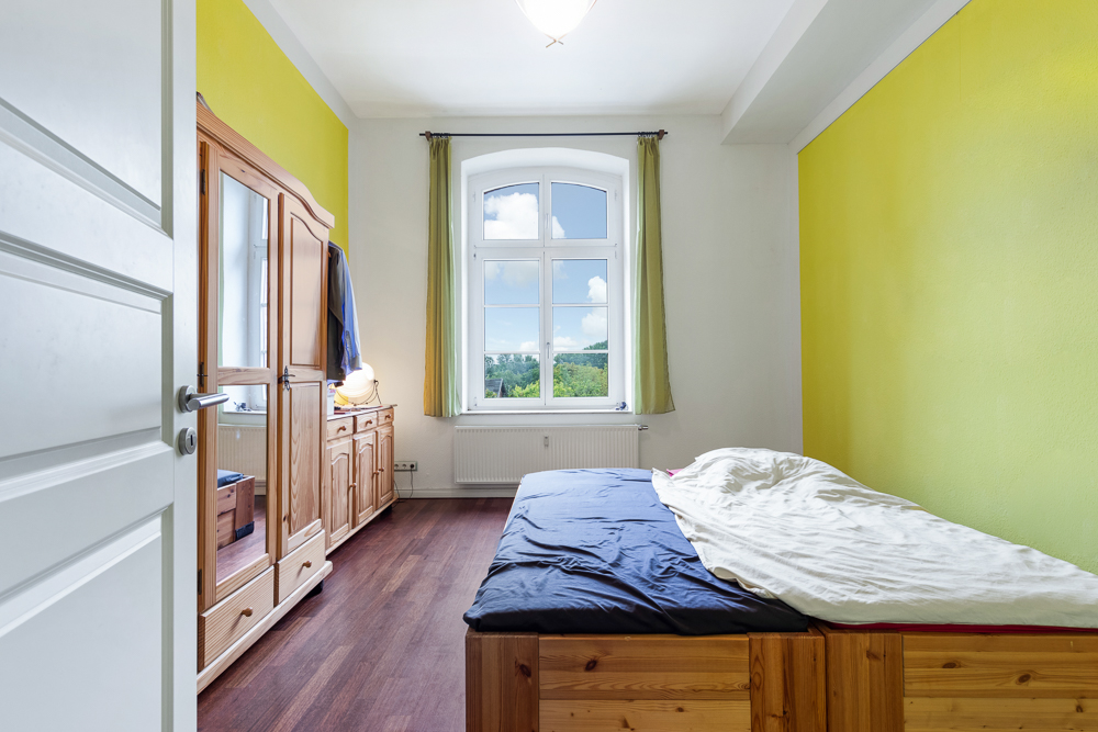 Helles Schlafzimmer mit Holzbett, Holzschrank und großem Fenster mit Blick nach draußen.