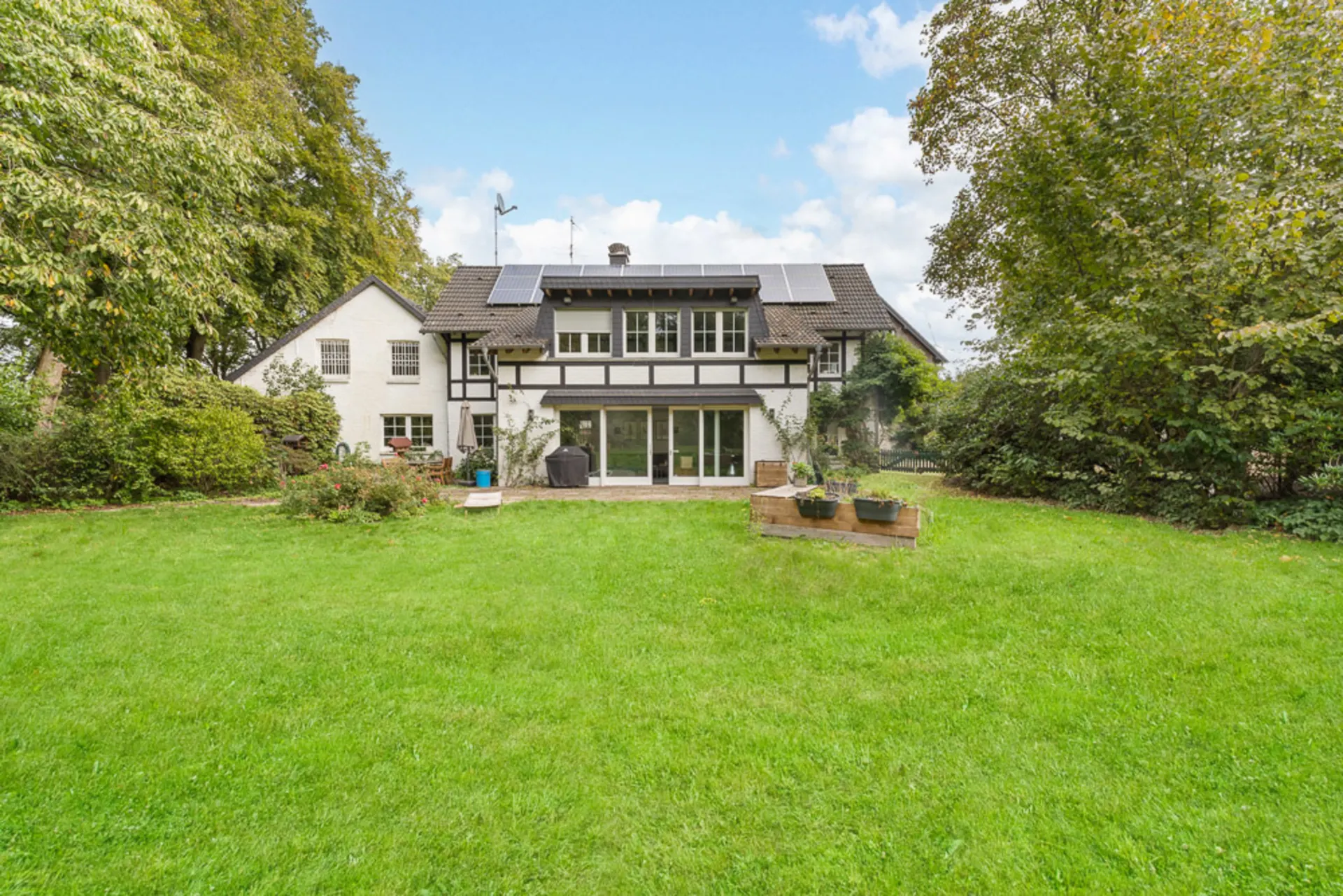 Fachwerkhaus mit Garten, Rasenfläche und mehreren Solarpanelen auf dem Dach.