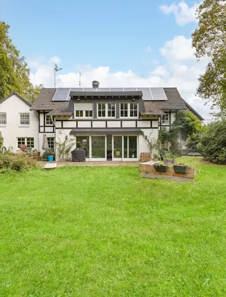Fachwerkhaus mit Garten, Rasenfläche und mehreren Solarpanelen auf dem Dach.