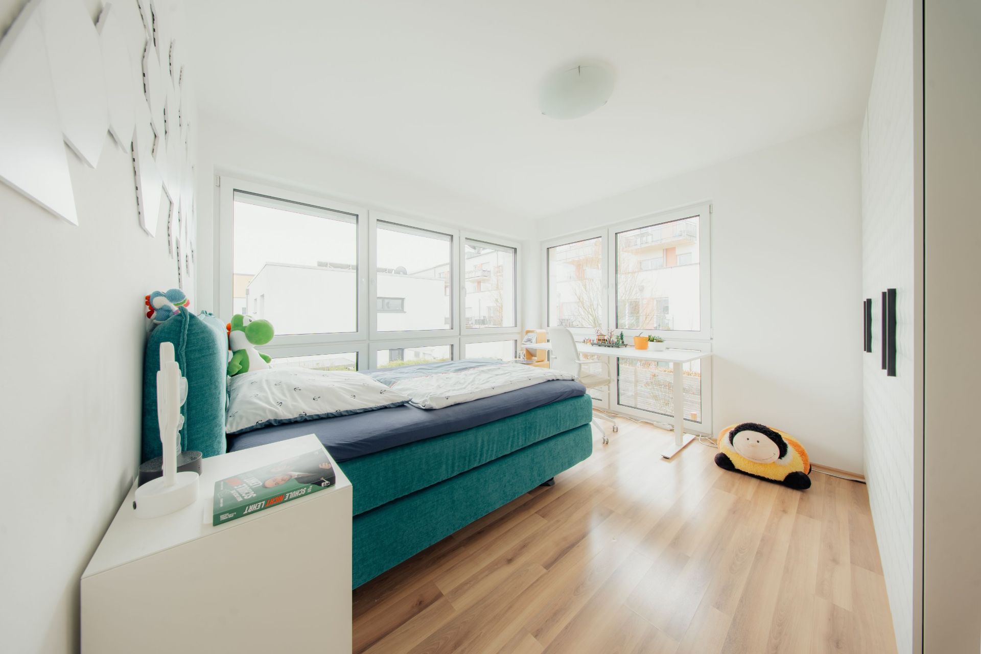 Helles Schlafzimmer mit großem Bett, Schreibtisch am Fenster und Holzfußboden.