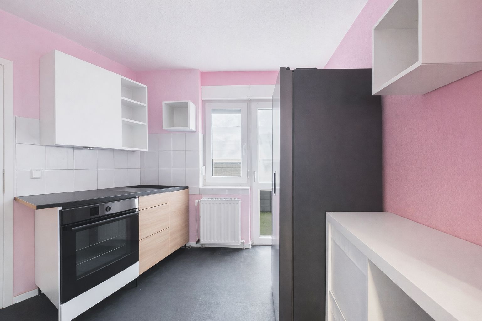 Moderne Küche mit pinken Wänden, weißen Schränken, Herd, Kühlschrank und Fenster.