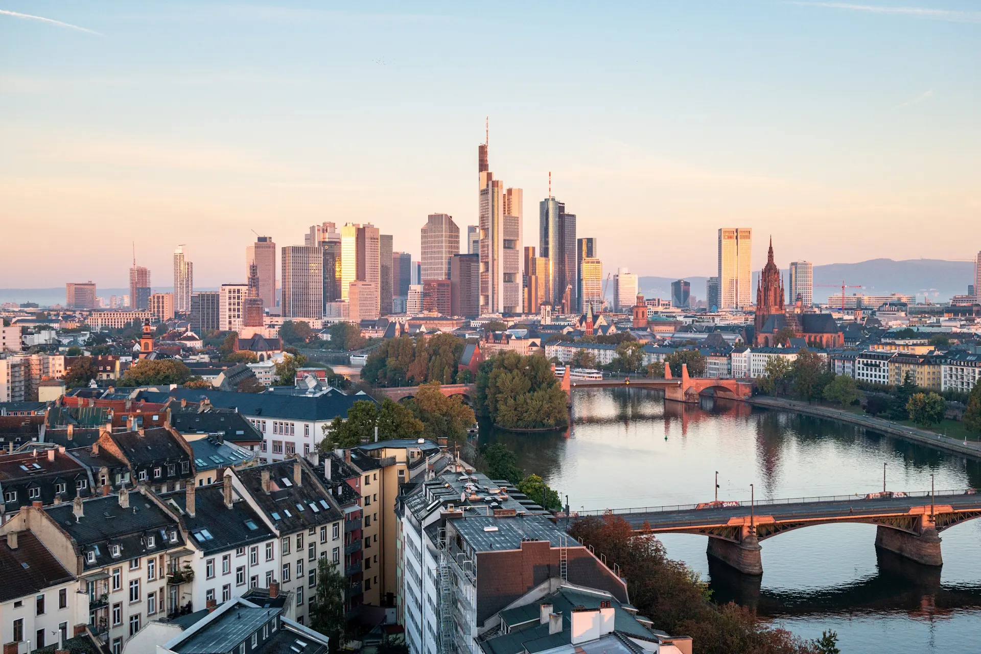 Blick auf Wohnhäuser, Fluss und moderne Hochhäuser im Hintergrund bei Sonnenuntergang.
