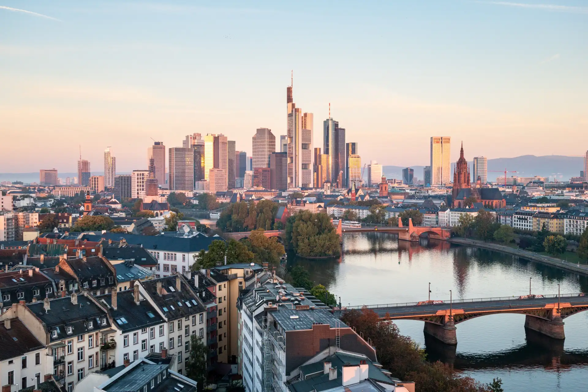 Blick auf Wohnhäuser, Fluss und moderne Hochhäuser im Hintergrund bei Sonnenuntergang.