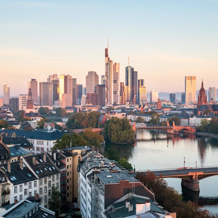 Blick auf Wohnhäuser, Fluss und moderne Hochhäuser im Hintergrund bei Sonnenuntergang.
