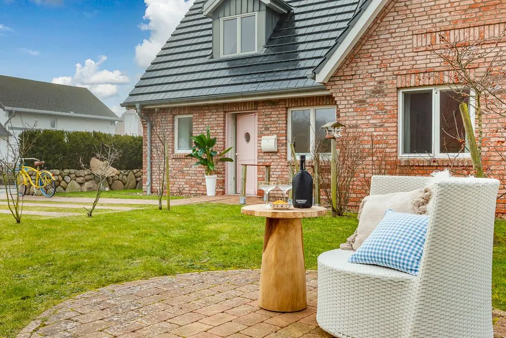 Gemütliche Terrasse mit Stuhl, rundem Holztisch und Blick auf ein Backsteinhaus mit Garten.