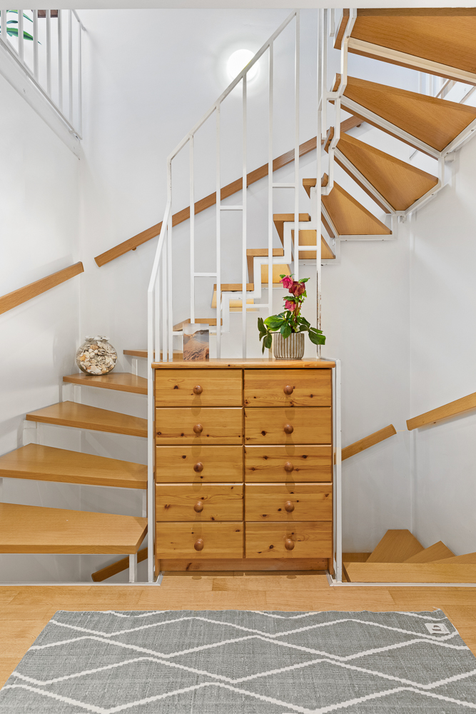 Holzkommode vor einer modernen, offenen Holztreppe in einem hellen Flur.