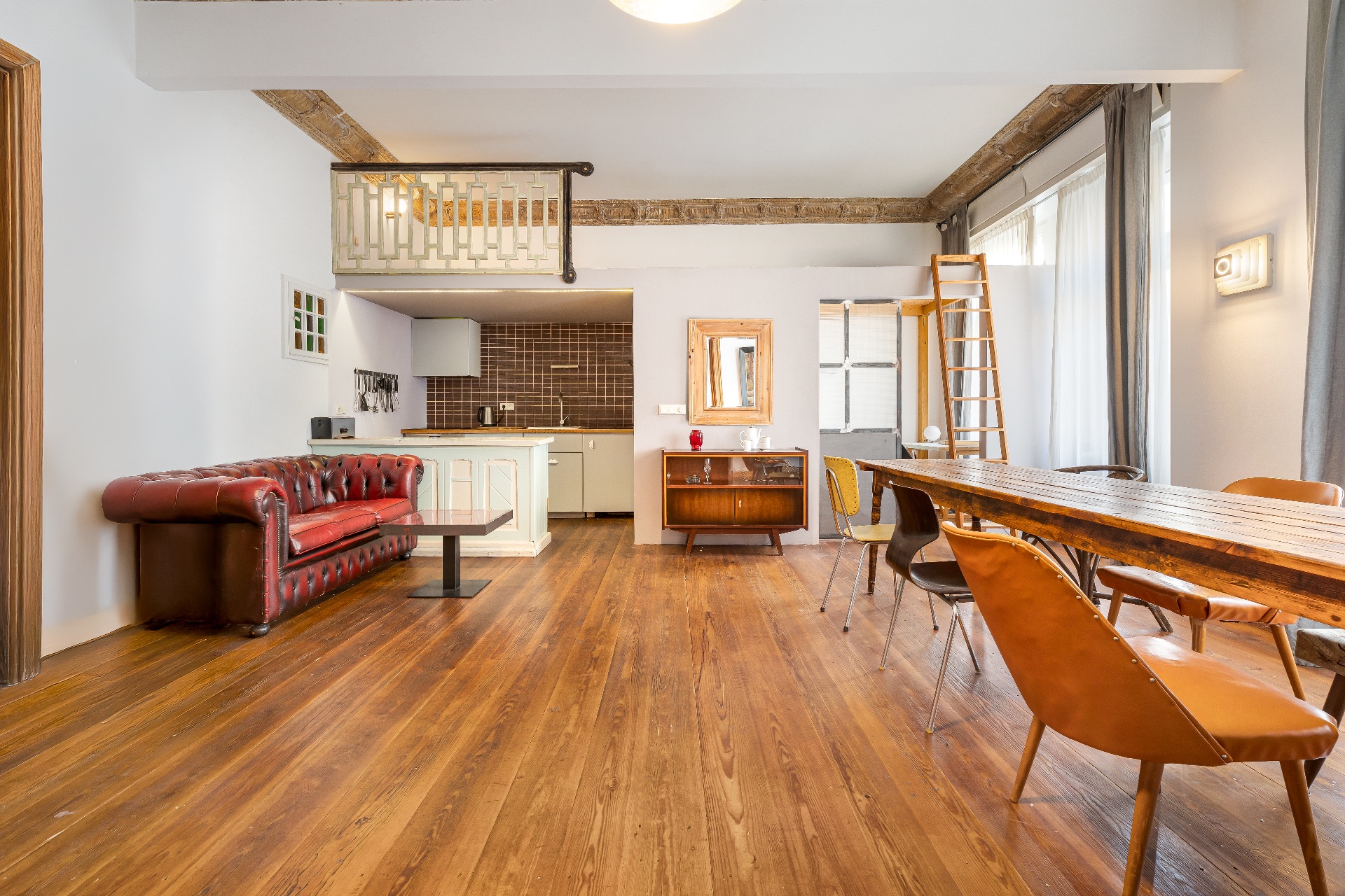 Helles Wohnzimmer mit rotem Ledersofa, Esstisch, Stühlen und offener Küche mit Holzfußboden.