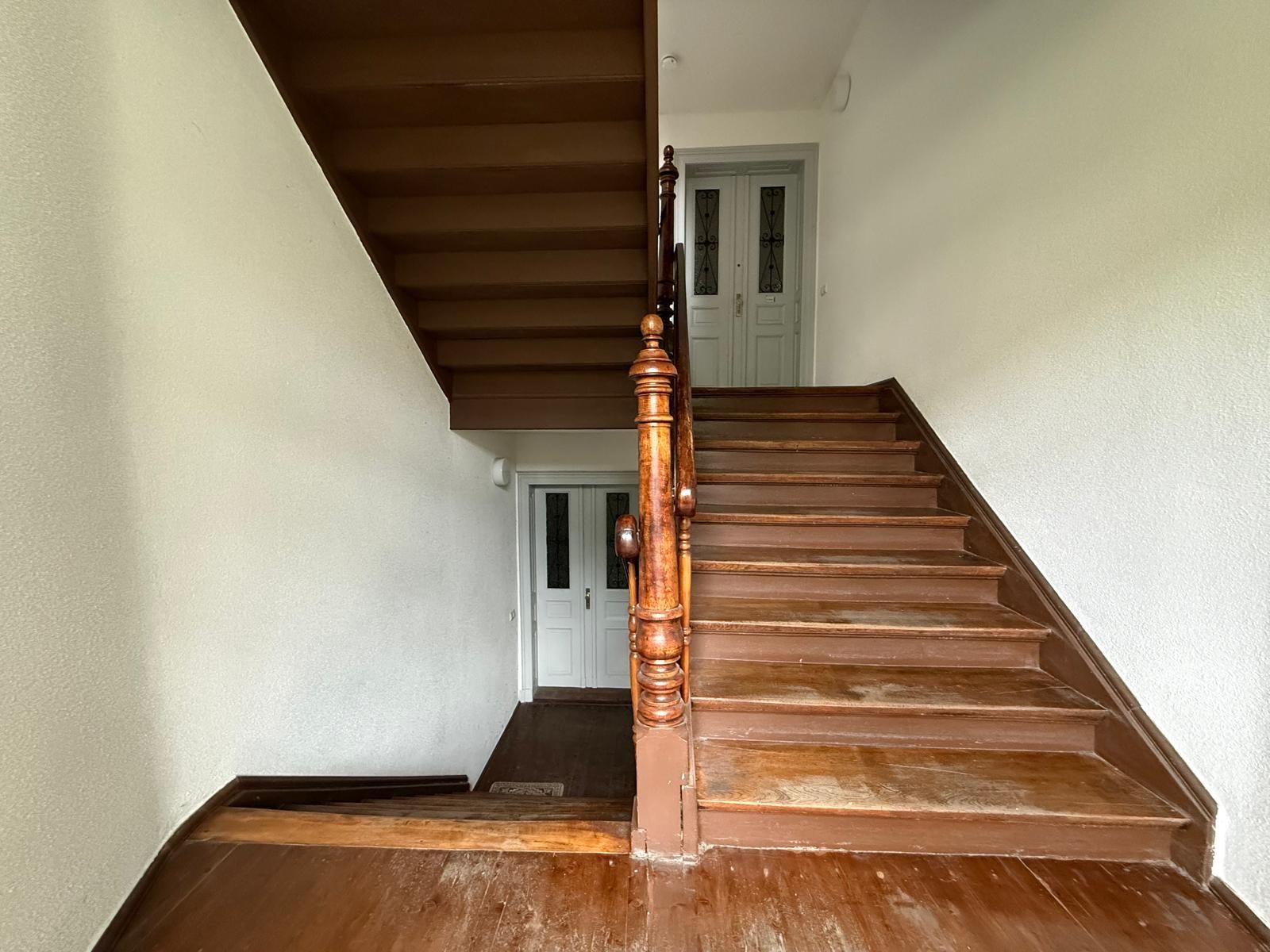 Holztreppenhaus mit weißen Wänden und zwei weißen Türen auf jeder Etage.