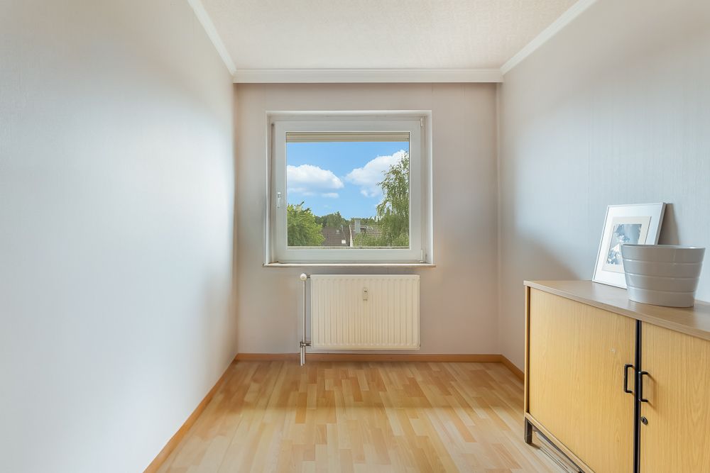 Helles, kleines Zimmer mit Fenster, Holzfußboden und Kommode, Blick nach draußen.