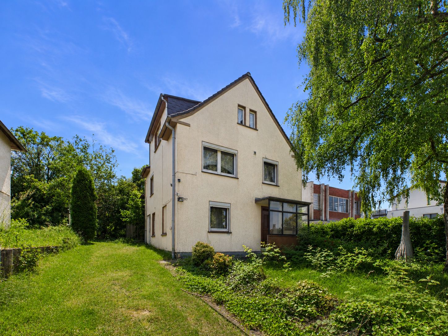 Zweistöckiges Wohnhaus mit Giebeldach und Garten, umgeben von Rasen und Bäumen.