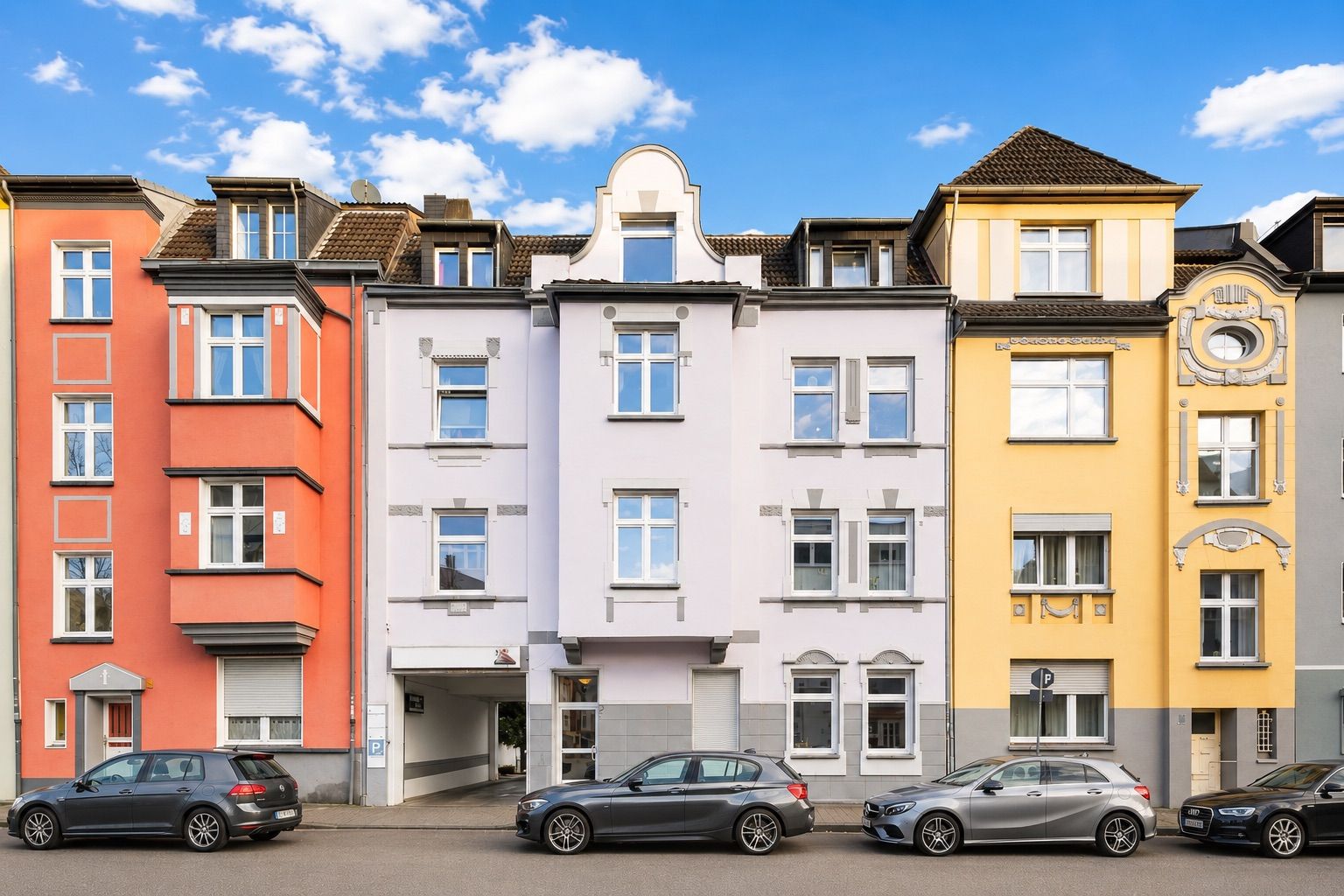 Mehrstöckige Wohnhäuser mit bunten Fassaden und geparkten Autos auf der Straße.