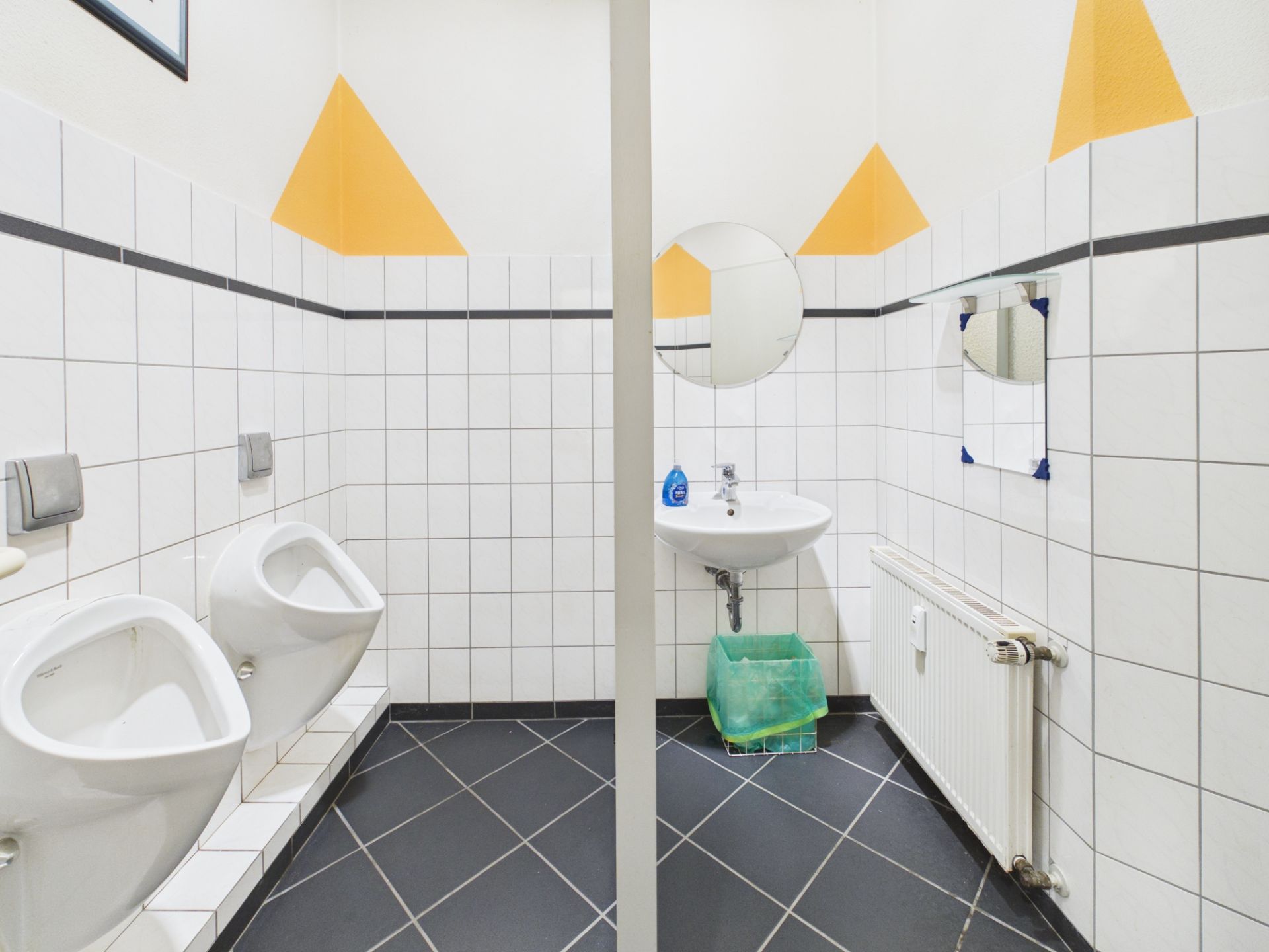 Heller, gefliester Waschraum mit zwei Urinalen, einem Waschbecken und zwei Spiegeln.