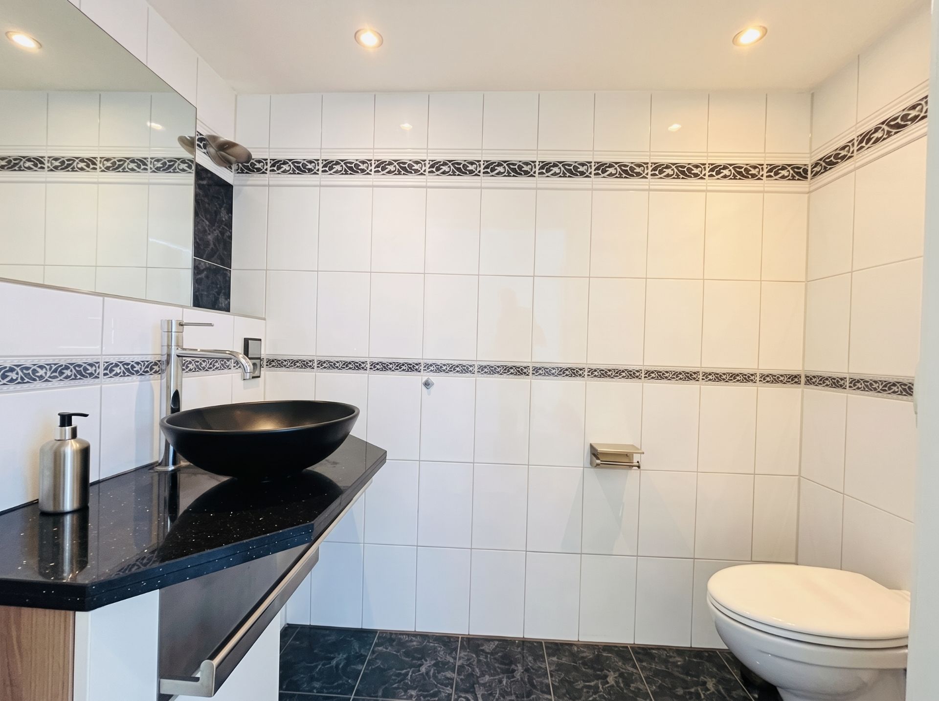 Modernes Badezimmer mit schwarz-weißem Waschbecken, Spiegel und Wandtoilette.