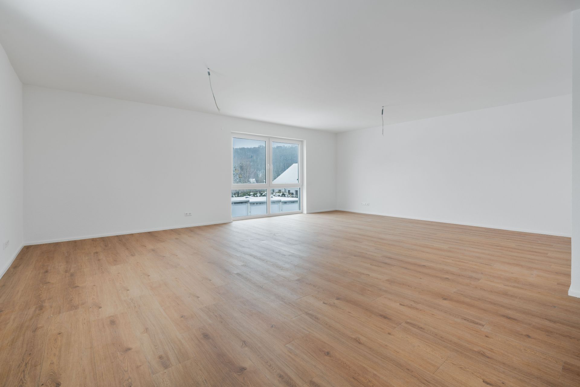 Leerer, heller Raum mit Holzfußboden und großen Fenstertüren zu einem Balkon.