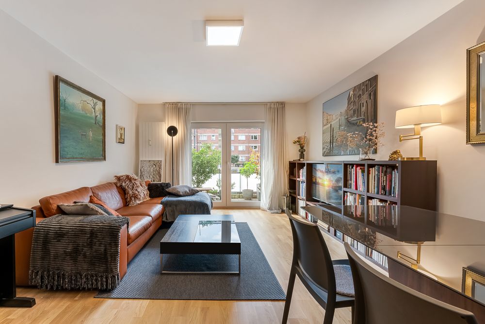 Modernes Wohnzimmer mit Ledersofa, großem Fenster, Bücherregal und Esstisch.