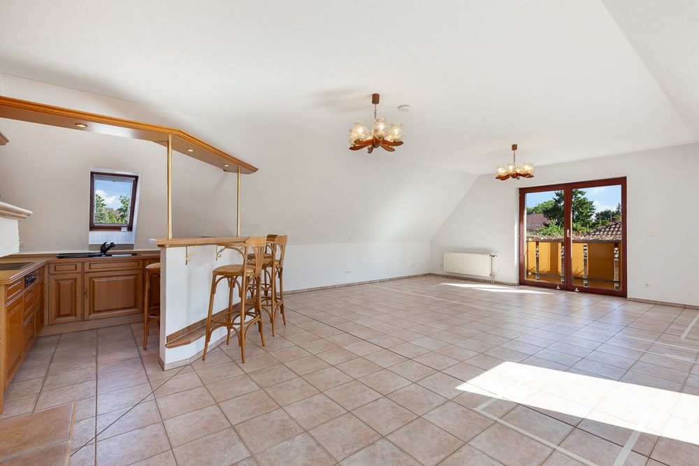Heller Raum mit offener Küche, Tresen, Fliesenboden und Zugang zum Balkon.