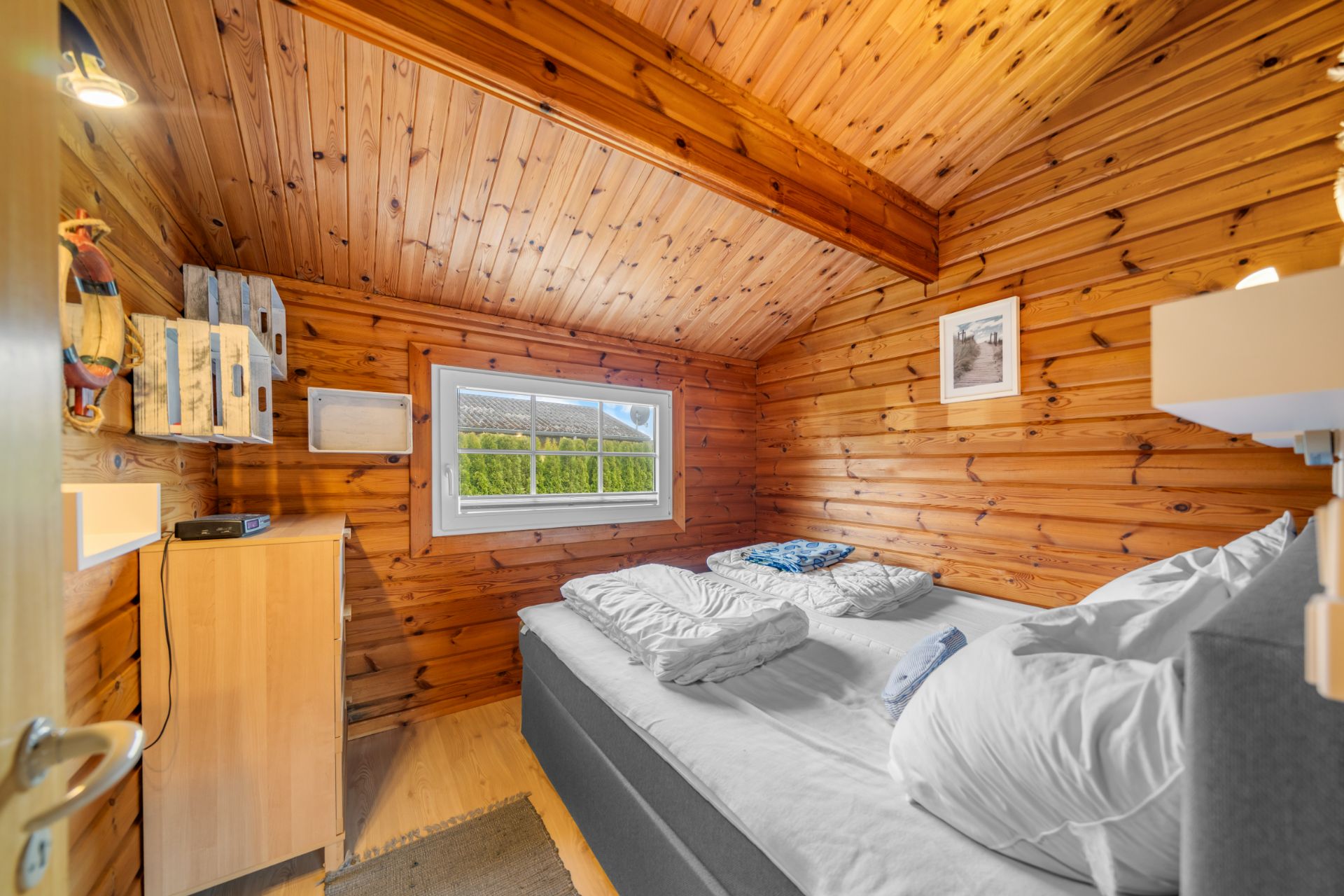 Kleines Schlafzimmer mit Holzwänden, Doppelbett und Fenster.