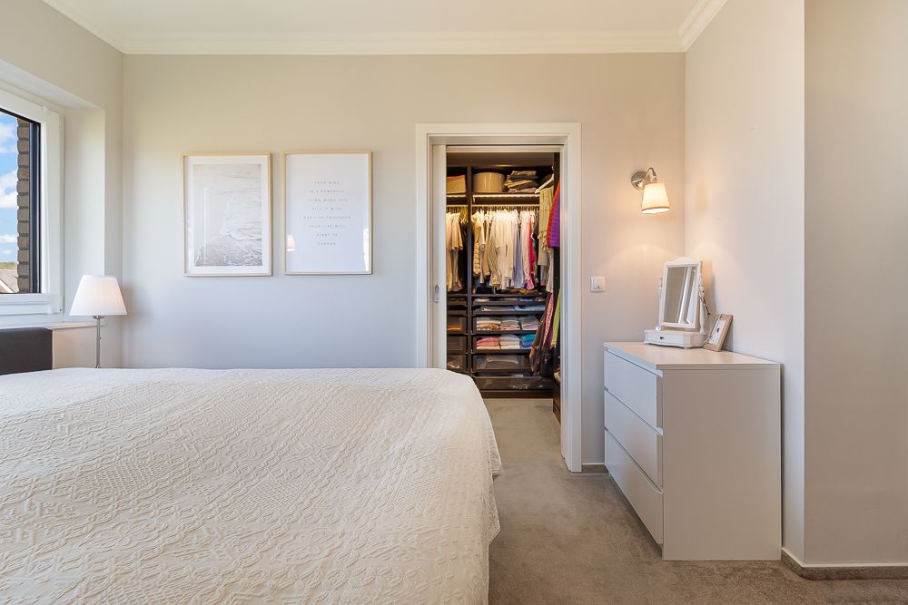 Helles Schlafzimmer mit Bett, Kommode und begehbarem Kleiderschrank.