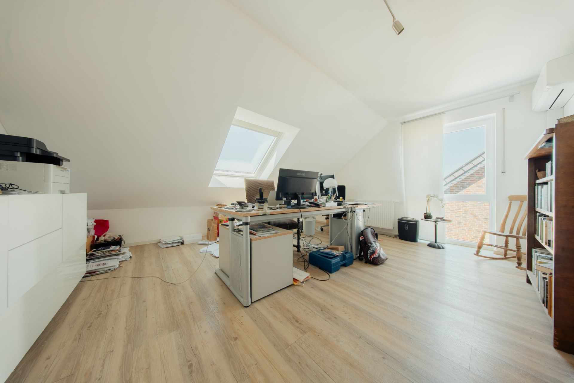 Helles Arbeitszimmer im Dachgeschoss mit Schreibtisch, Computer, Stuhl und Bücherregal.