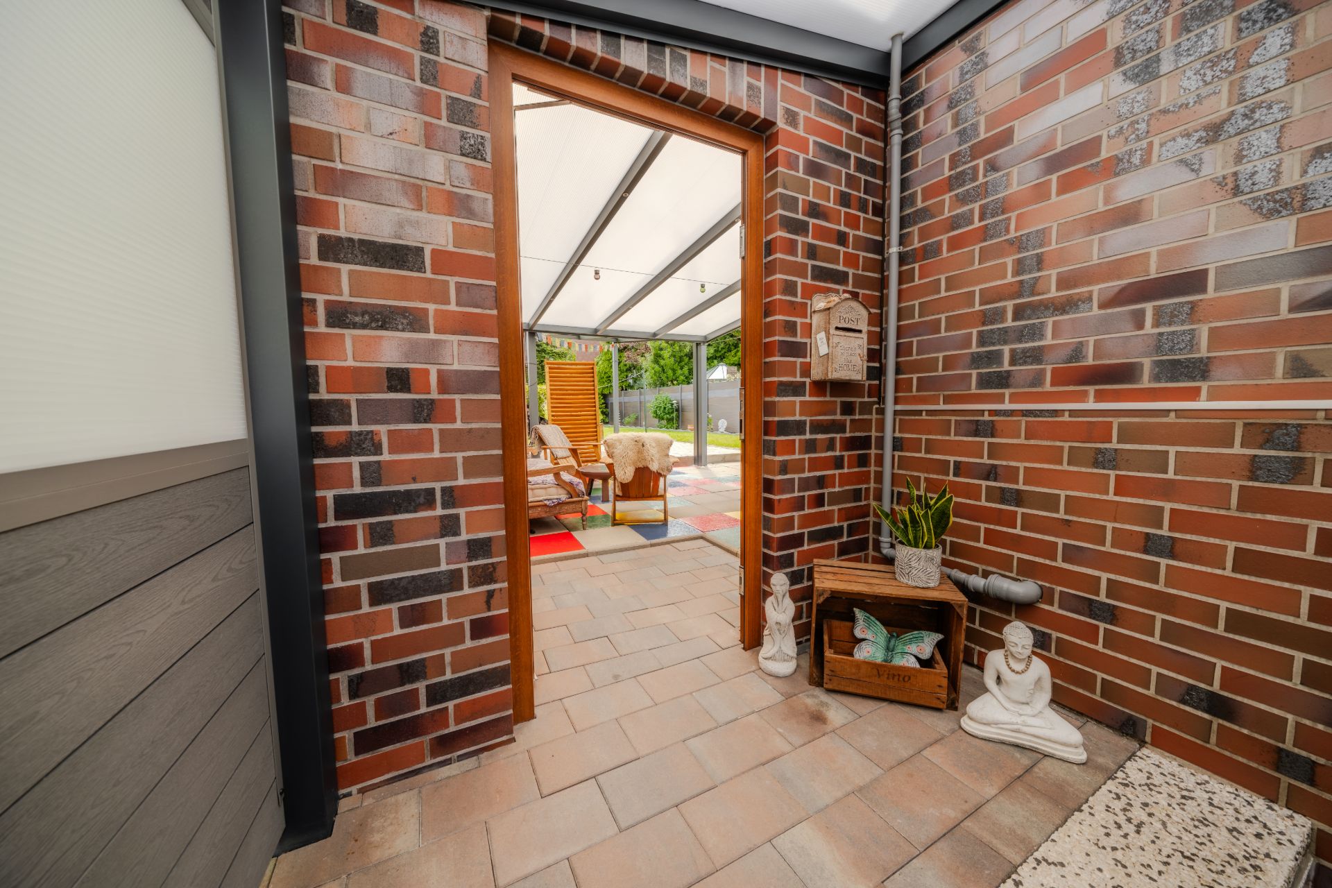 Offener Durchgang von Flur zu verglaster Terrasse mit Holzmöbeln und Dekorationen.