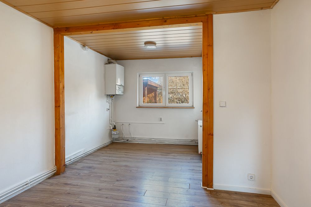 Leerer Raum mit Holzdecke, Laminatboden, weißer Wand und zwei Fenstern.
