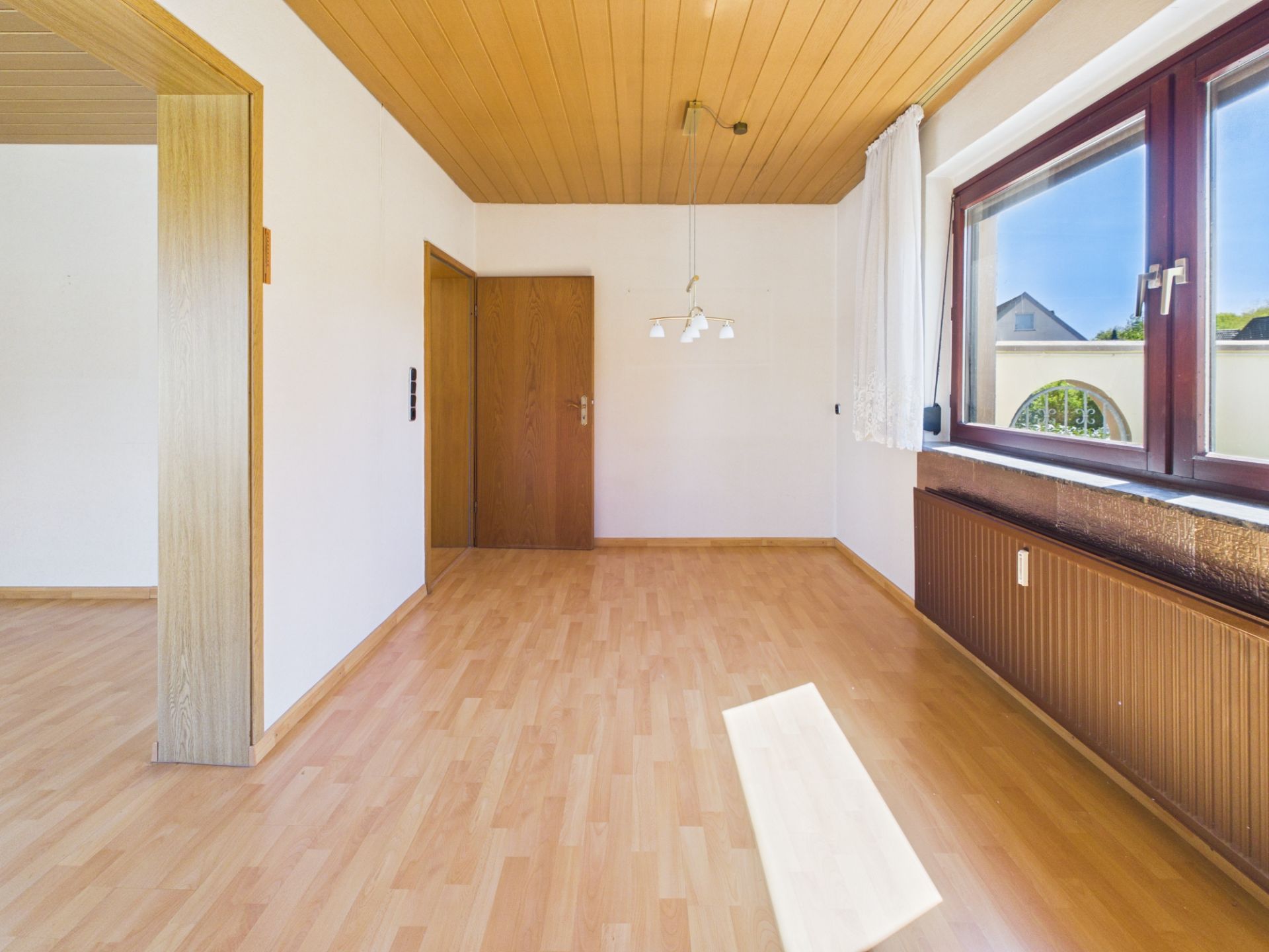 Leerer Raum mit Holzboden, Holztür, großem Fenster und Heizung unter dem Fenster.