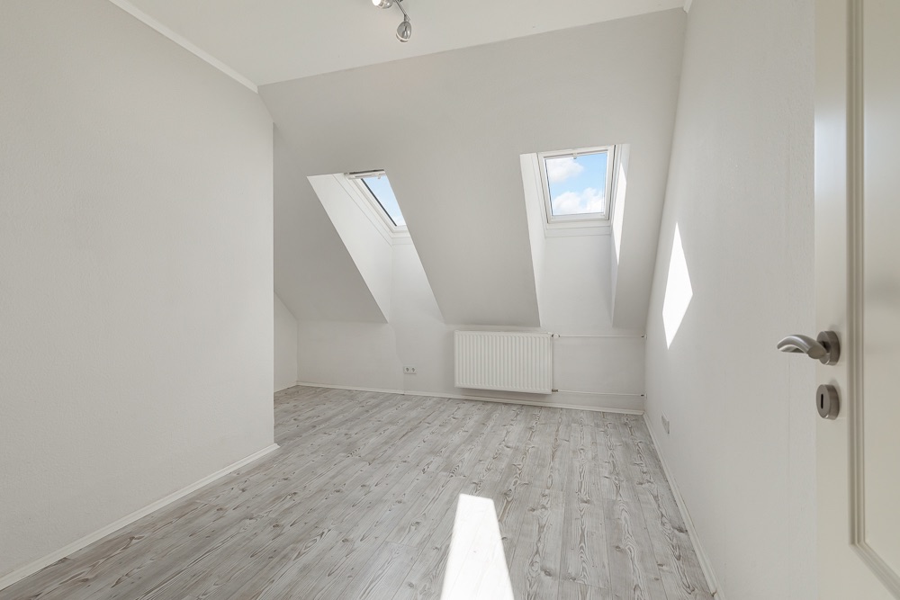 Heller Raum mit schräger Decke, zwei Dachfenstern und hellem Holzboden.