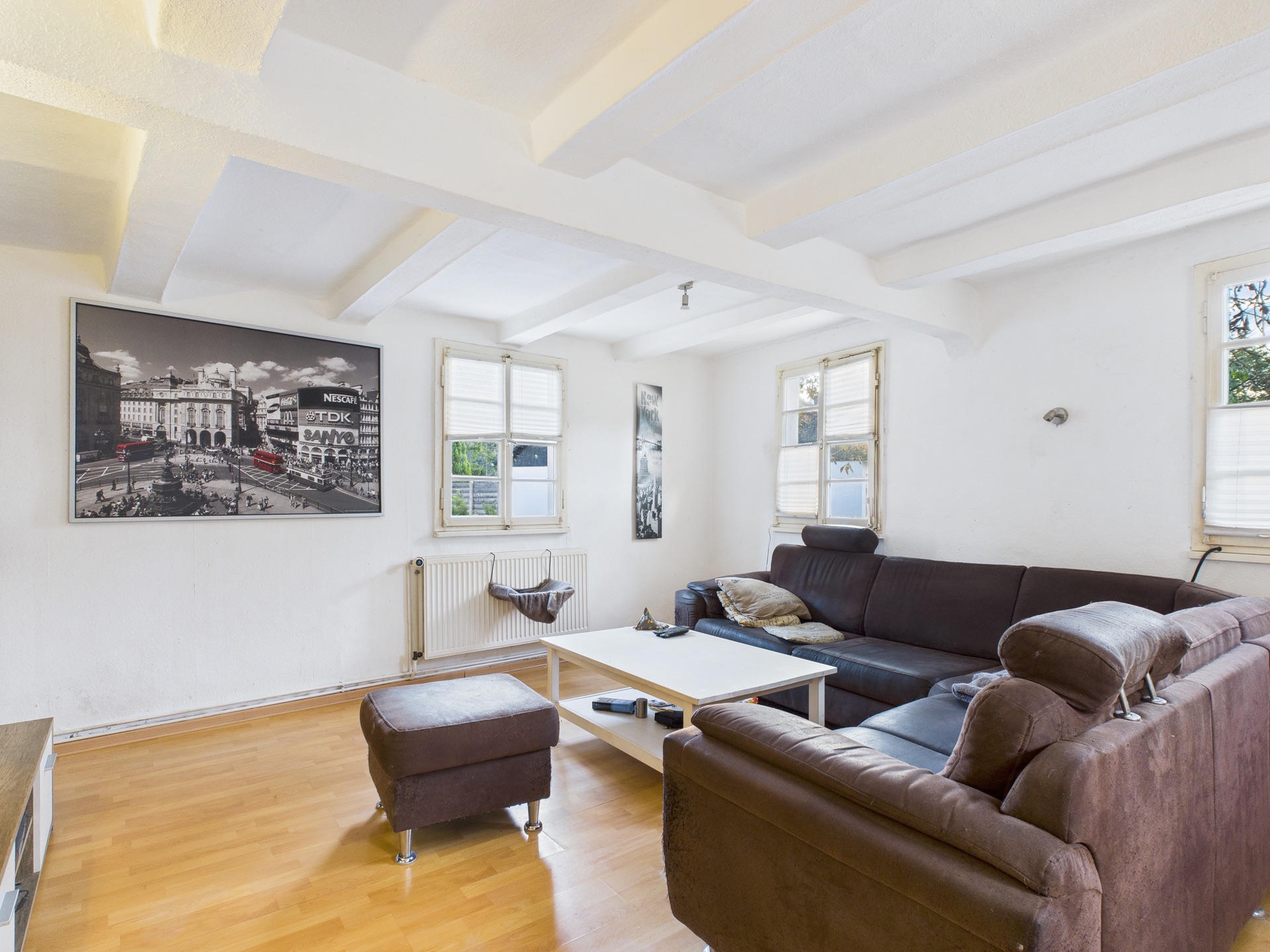 Wohnzimmer mit braunem Ecksofa, Couchtisch, Hocker und großen Fenstern.