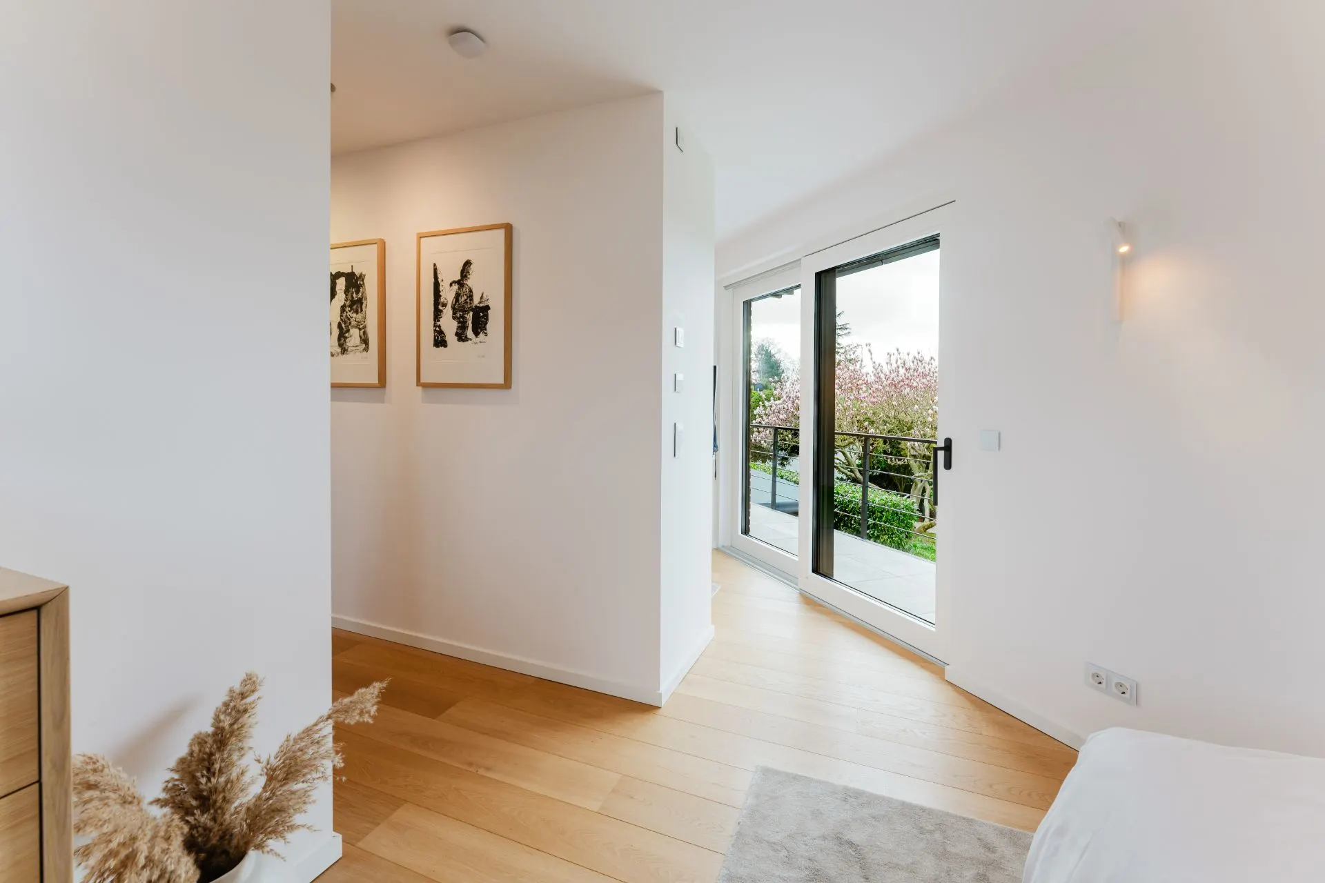 Helles Zimmer mit Holzboden, Glas-Schiebetür zum Balkon und zwei Bildern an der Wand.