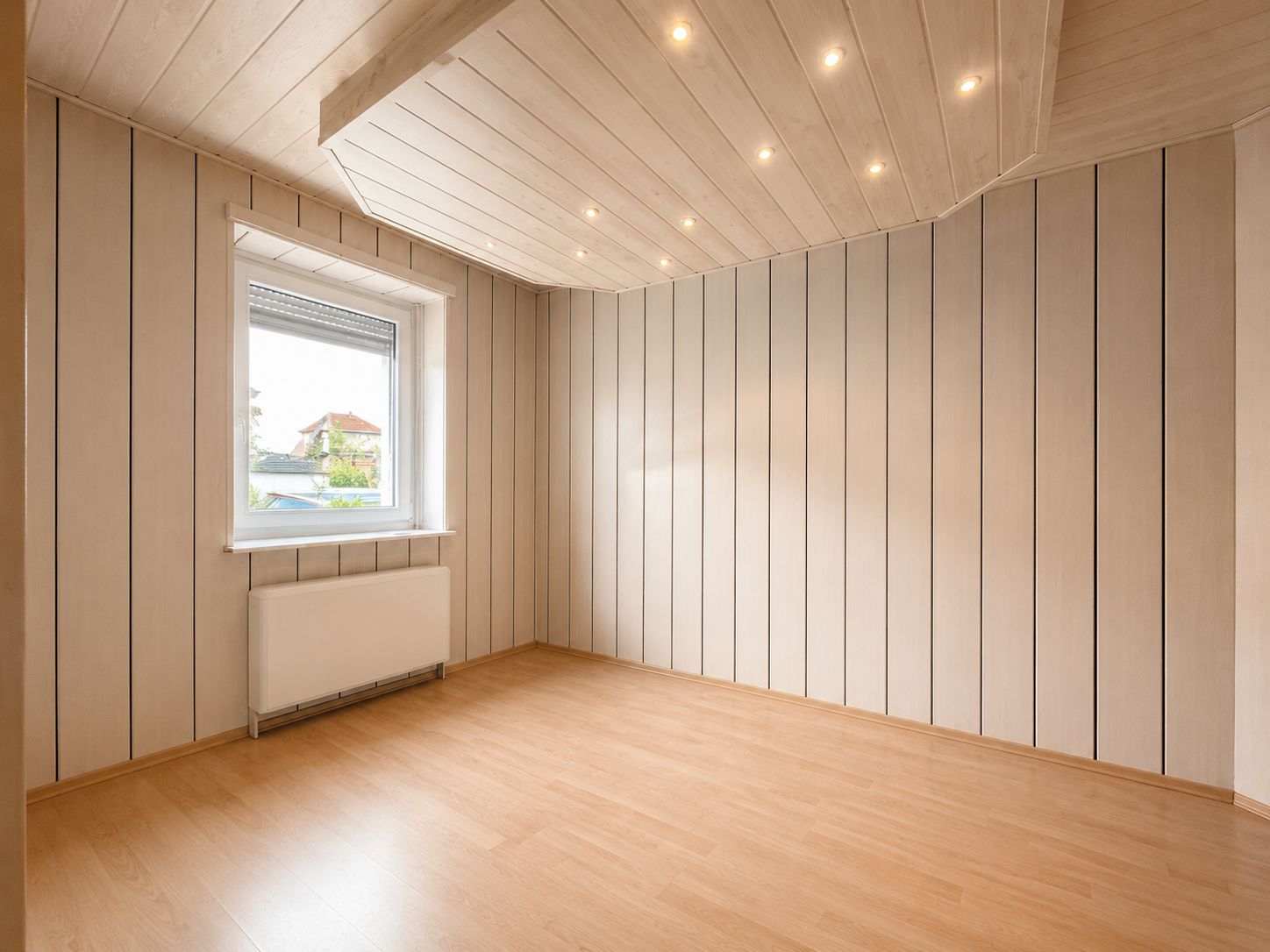 Leerer Raum mit Holzlaminatboden, vertikal getäfelten Wänden und Fenster mit Blick nach draußen.