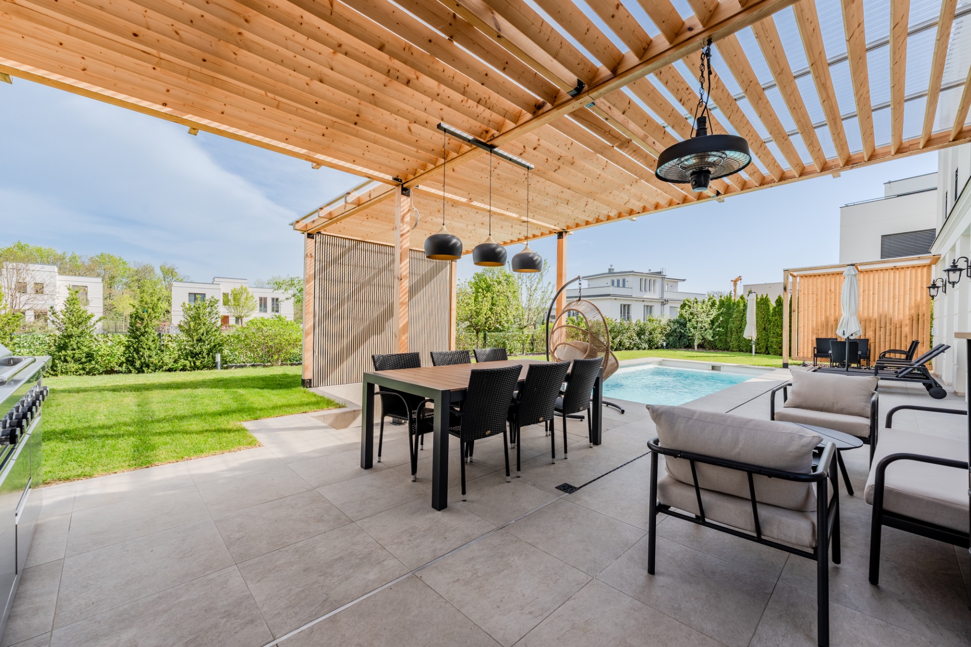 Überdachte Terrasse mit Esstisch und Stühlen, daneben ein Pool im Garten.