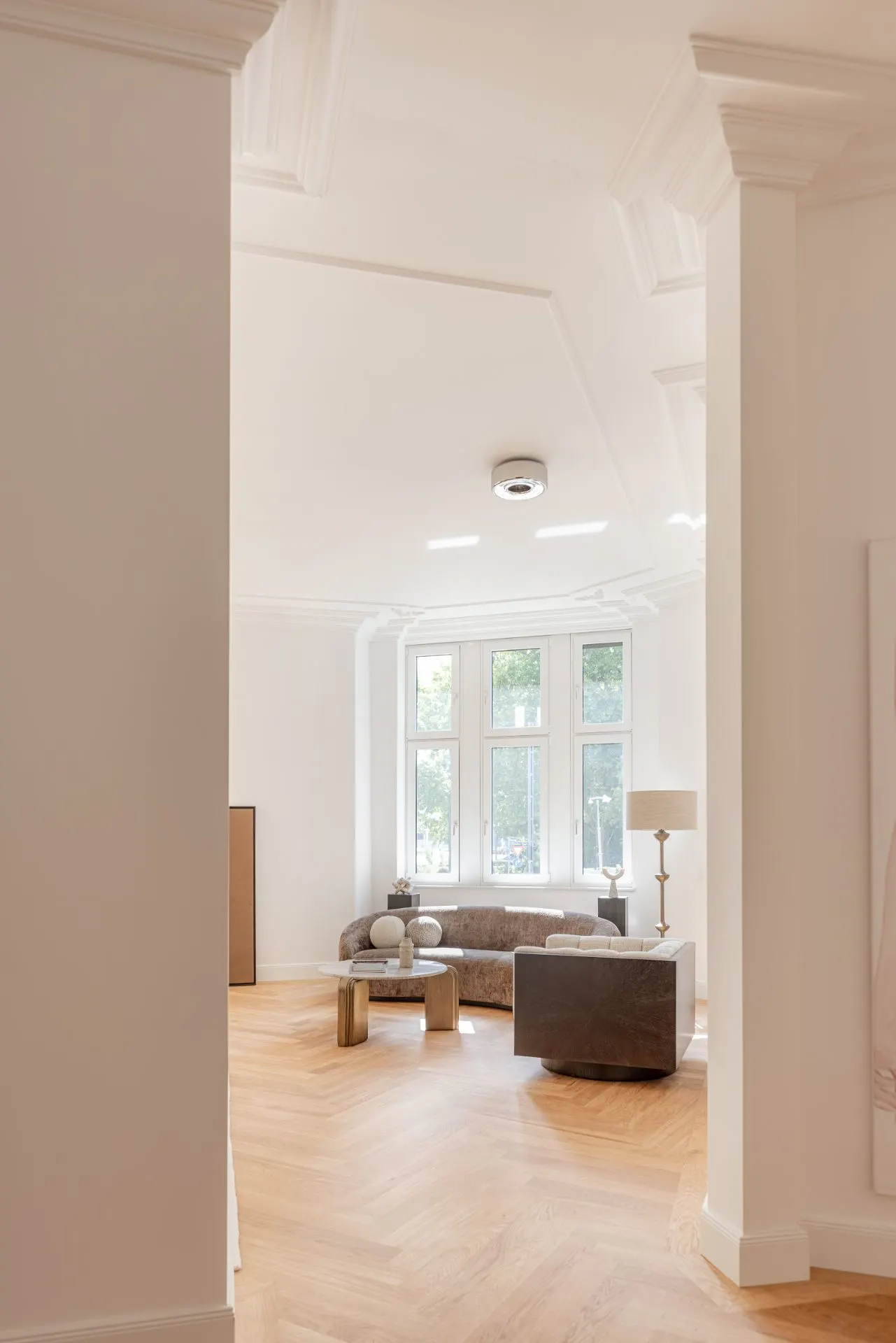 Helles Wohnzimmer mit Parkettboden, Fensterfront, Sofa, Sessel, Stehlampe und Couchtisch.