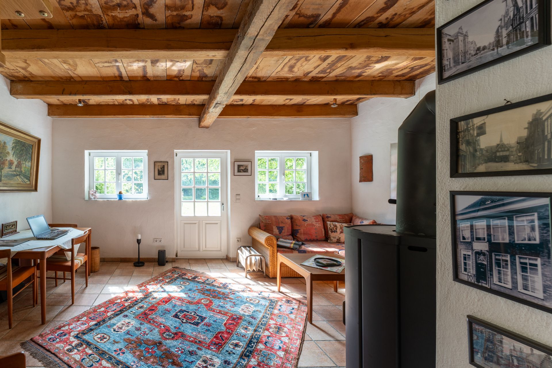 Helles Wohnzimmer mit Holzdecke, Sofa, Teppich, Esstisch und Wandbildern.